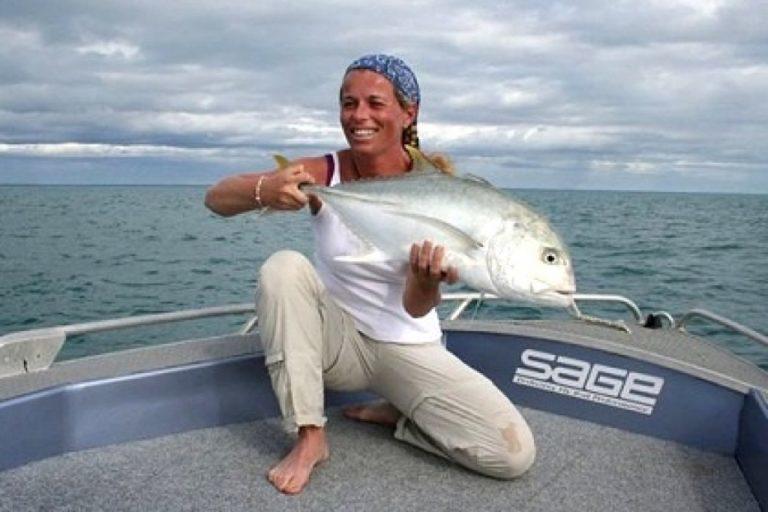 A frontal landscape shot of a woman holding up her catch. She is wearing a High UV Buff® as hair cover. The photo is taken in Far North Queensland so it is hot and humid. The boat is a professional fishing charter vessel. It looks as if she has been out fishing all day and is really happy about her catch. Source: flyfishingweipa.com.au Copyright: Permitted to use on our website
