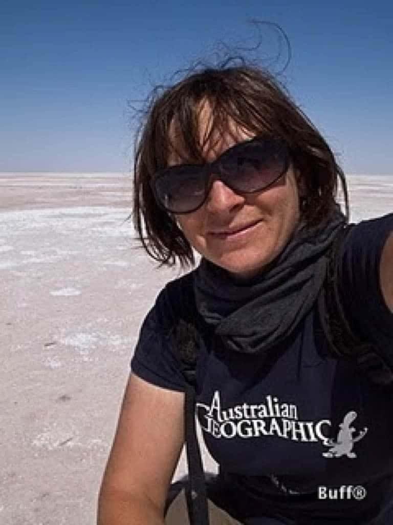 A portrait selfie of Danielle Murdoch somewhere in the middle of nowhere. She is wearing a short sleeve Australian Geographic T-shirt and a grey Wool Buff® as scarf. The hair looks a bit scruffy as if she just took her motorcycle helmet off. She appears to be in her comfort zone and looks happy. Source: Danielle Murdoch motomonkeyadventures.com © permission to use on our websites