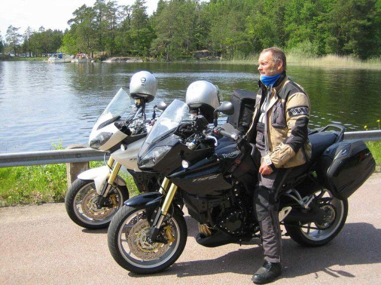 A side landscape shot of a man sitting on his touring motorcycle. It is the Norwegian Buff® distributor on a tour through Norway. He wear full motorycle touring gear and a blue Original Buff®. Look closer and you can see the Buff® as scarf around the neck with the top pulled up over the chin. The weather looks like Norwegian Summer. Nice but on the cooler side. Source: buff.eu Copyright: Distributed for the promotion of the Original Buff® in motocycle touring