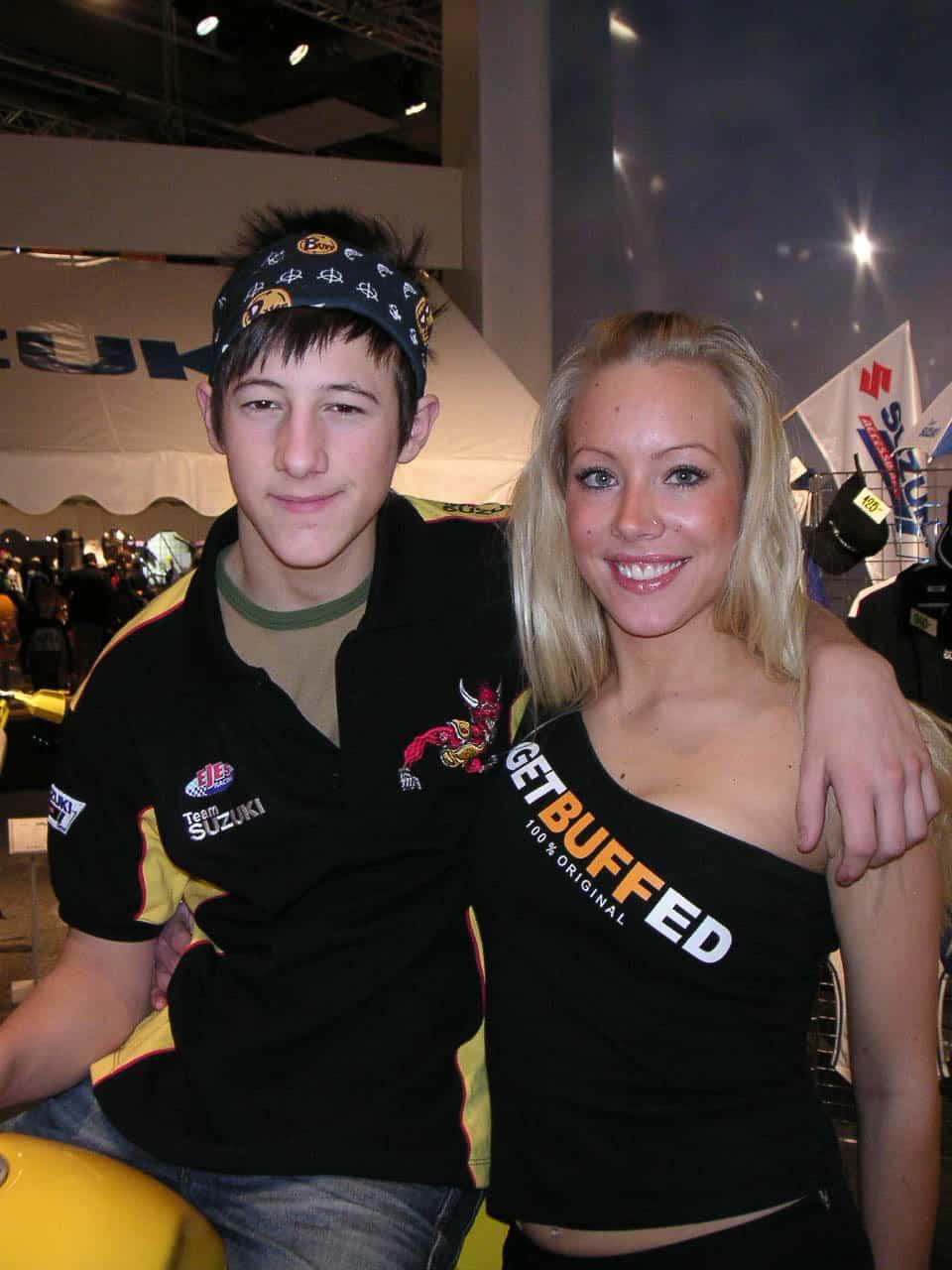 A portrait frontal upper body photo of a you man and woman on a motorcycle trade show. The man on the left is sitting on a motorbike and the woman is standing to the right. The woman seems to be a promo girl for Buff® and the man seems to be a Suzuki team rider. He is wearing a Original Buff® as head band in a very stylish, expressive way. Source: buff.eu Copyright: Distributed for the promotion of Original Buff® in motorcycling