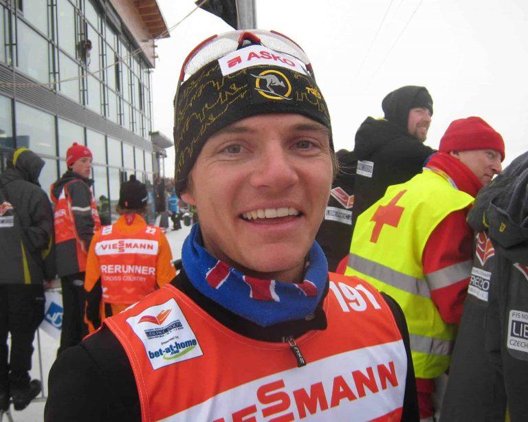 A landscape frontal shot of a joung XC skiing athlete before a race. It's Ben Sim smiling into the camera during the 2009 World Championships. He is wearing a Australian Flag Original Buff® as warming scarf. This way sweat doesn't cause any chill around the neck. Source: Finn Marsland © permission to use on our websites for the promotion of the Original Buff® in cross country skiing