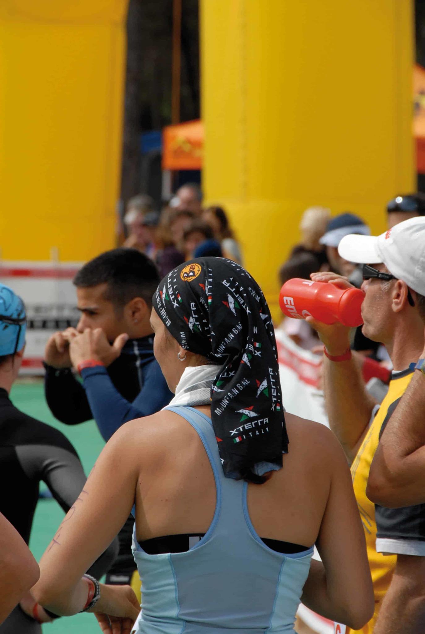 A back portrait shot of a woman standing in a triathlon race crowd. She is wearing a High UV Buff® as hair cover. This is a way to tame and dry your wet hair after the swim. Source: buff.eu © distributed for the promotion of the High UV Buff® in running / triathlon