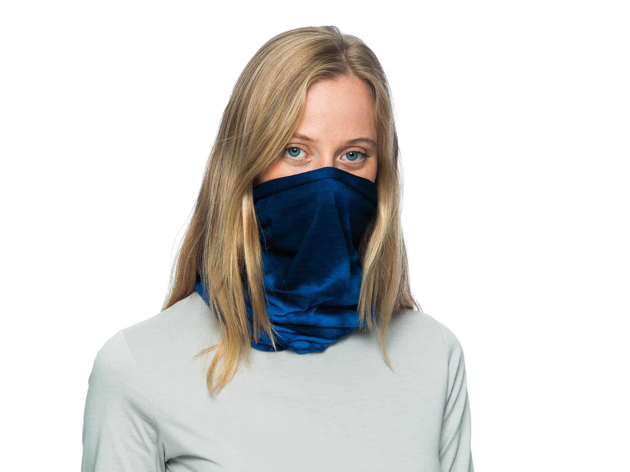 A studio landscape shot of a young woman wearing a Wool Buff® as face mask. She is blond, wearing a white shirt & standing in front of a white background. The tye-died blue Wool Buff® stands out. Source: buff.eu © Distributed for the promotion of the Wool Buff®