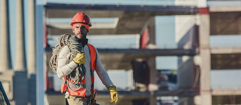 Photo of a male construction worker wearing a Buff® Professional Thermal Hat under his hard hat. The colours indicate that it is cold on site. In the background you can see a multi story development in it's raw concrete state. Source: buff.eu