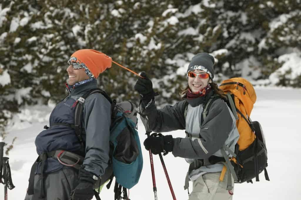 A man and a woman walking in winter sport gear through the snow. The woman is walking behind the man and pulling a drawstring on his Buff® Polar Neckwarmer. The photo is a photoshoot for the promotion of the Buff® Polar Neckwarmer. Source: buff.eu