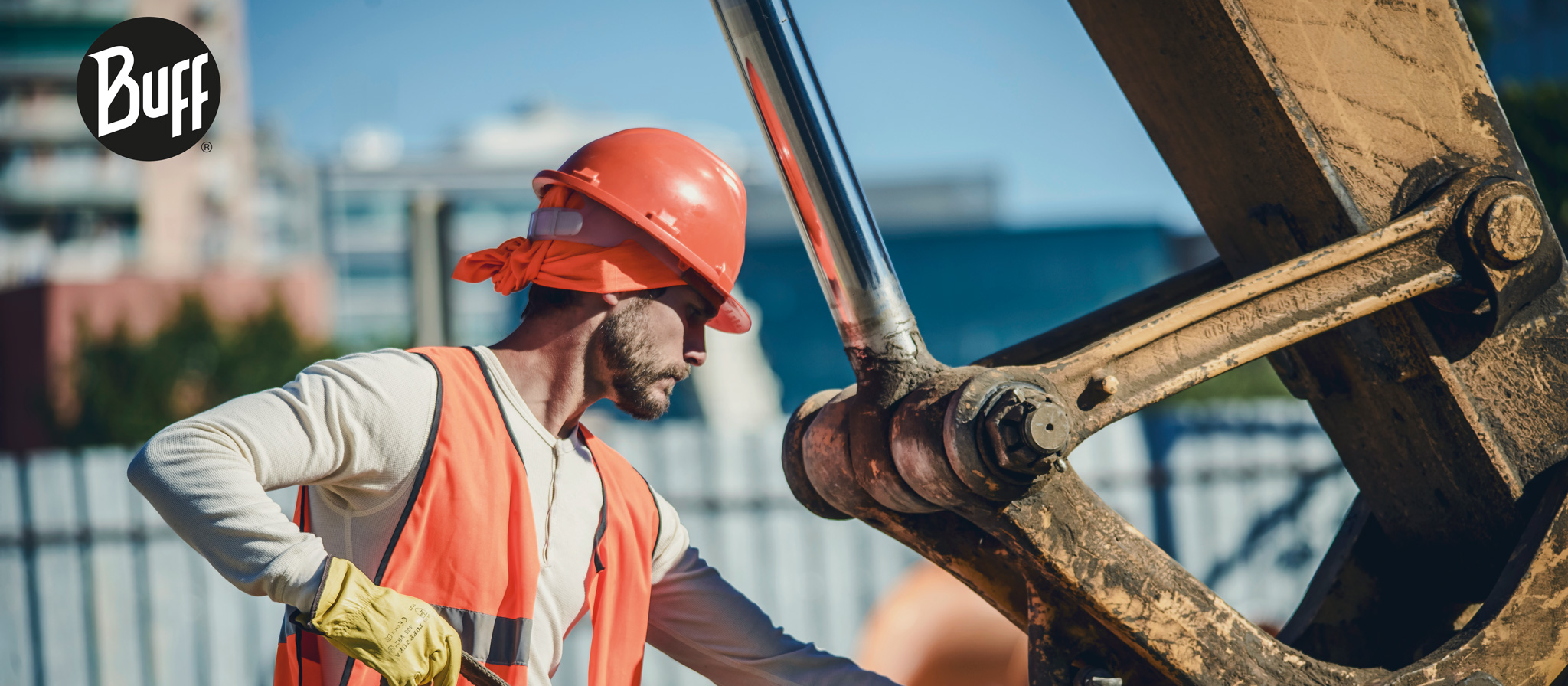 The image shows a construction worker using a Dry Cool or a Modacryl FR Buff® as helmet liner. The man is working on lifting gear with heavy machinery in the background. A Buff® trademark logo is placed on the top left corner. Source: buff.eu