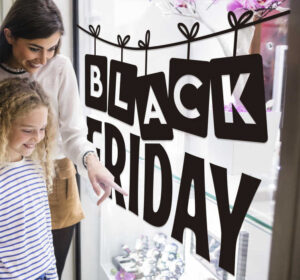 A mother and her daughter in front of a window display. The window has a "Black Friday" Sticker all over it.