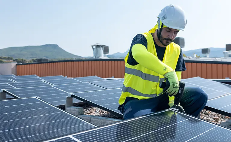 A man on a roof top installing solar panels. The Man is wearing the BUFF® Safety Arm Sleeves in yellow Fluor among other PPE. Source: buff.eu