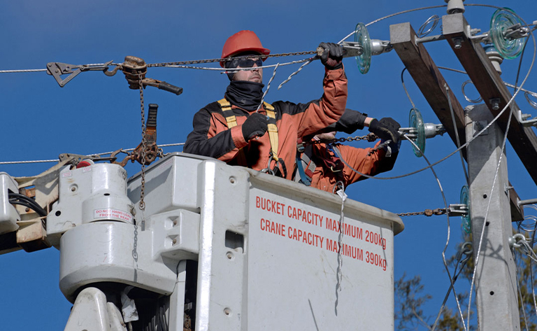 A high voltage transmission line specialist working in a scissor lift bucket on the maintenance of a high voltage transmission line.